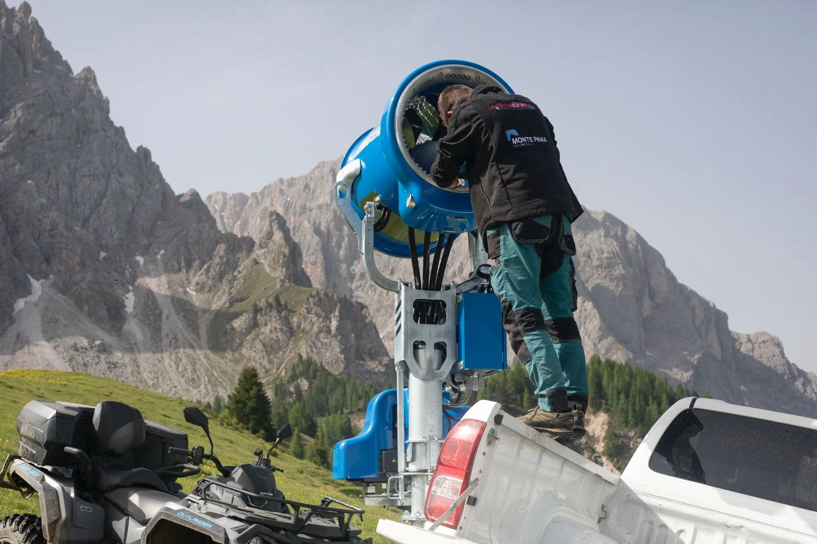 Ein Arbeiter der Monte Pana S.p.A. wartet eine Schneekanone. Die Kanone ist blau und im Hintergrund sind die Berge zu sehen